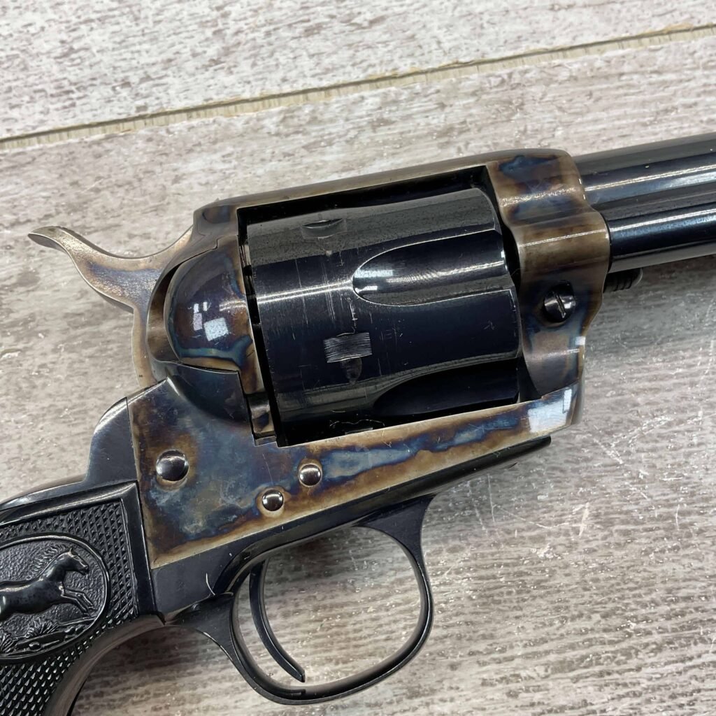 A vintage revolver with a dark metal finish, featuring intricate custom detailing, displayed on a light-colored wooden surface.