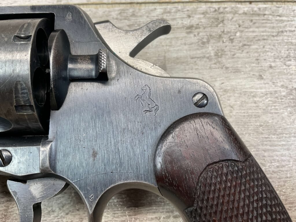 Metal revolver close-up with engraved horse logo, featuring a textured wooden grip and mechanical details.