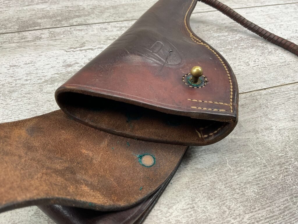 Vintage leather holster with a brass button, showing signs of aging, on a wooden surface. An authentic piece of historical military equipment, reflecting classic craftsmanship and design.