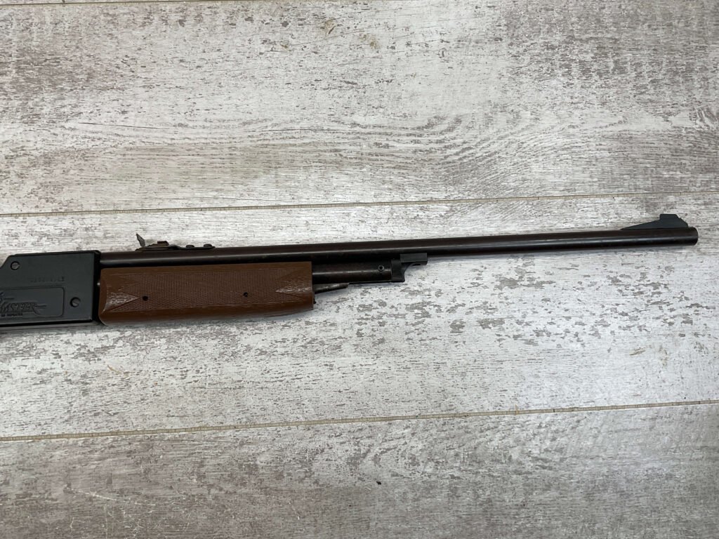 Air rifle with wooden stock, used for shooting practice or sport, placed on a wooden surfaceâ€”highlighting outdoor activity or hunting gear at Checkpoint Charlie's.